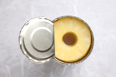 Open tin with canned pineapple on light grey marble table, top view