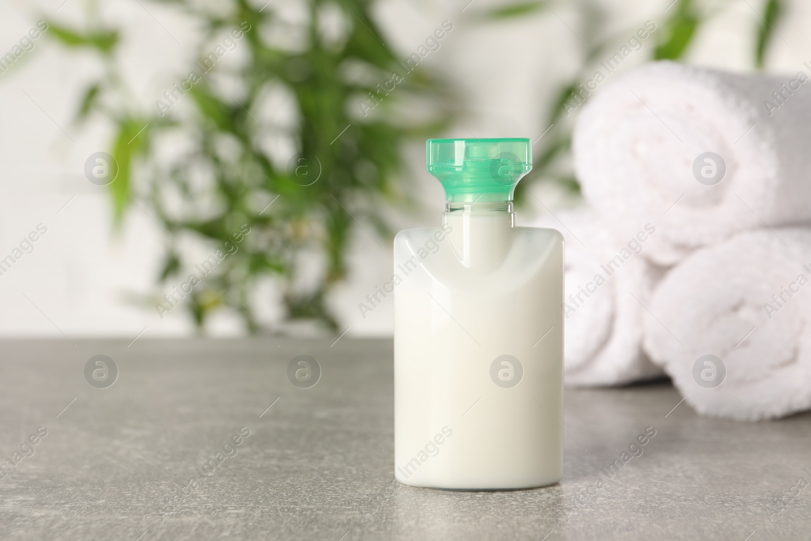 Photo of Mini bottle of cosmetic product and rolled towels on light grey table against blurred background. Space for text