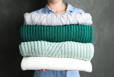 Photo of Woman holding stack of warm clothes on dark background, closeup. Autumn season