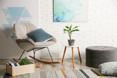 Comfortable rocking chair near brick wall in modern room interior