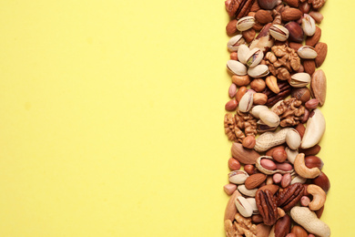 Different delicious nuts on yellow background, flat lay. Space for text