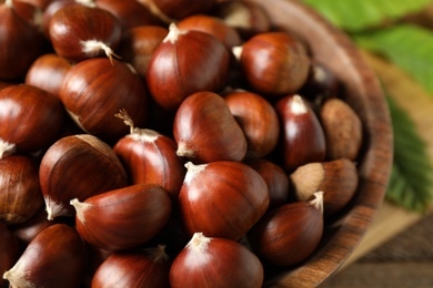 Photo of Fresh sweet edible chestnuts in wooden bowl, closeup