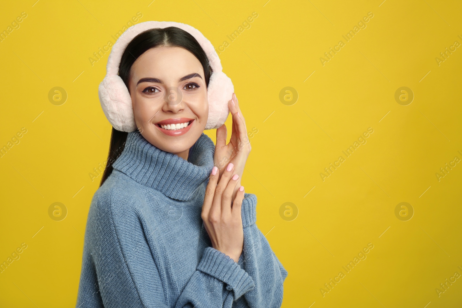 Photo of Beautiful young woman wearing earmuffs on yellow background. Space for text