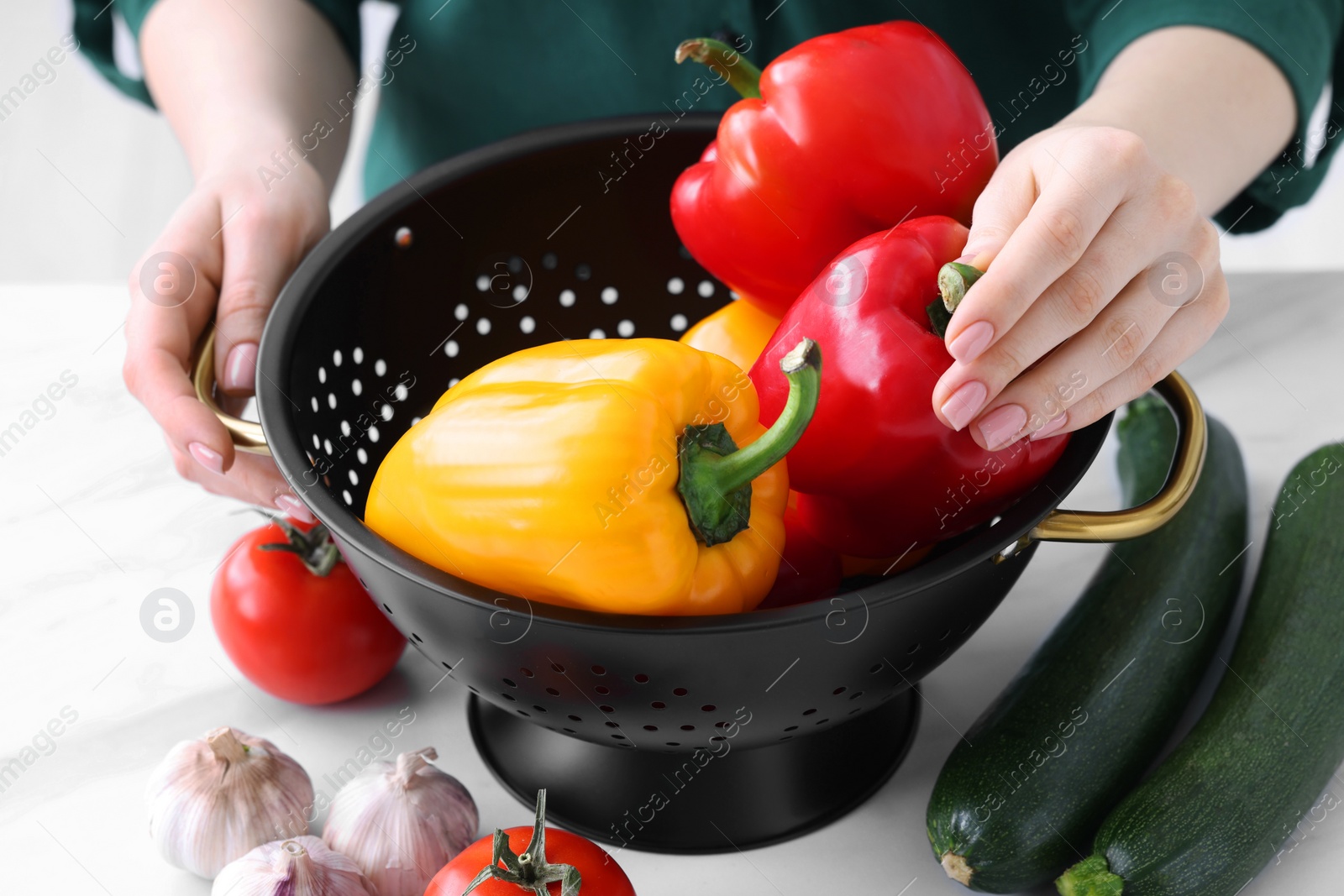 Photo of Woman taking bell pepper from black colander at white table, closeup