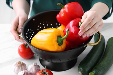 Woman taking bell pepper from black colander at white table, closeup