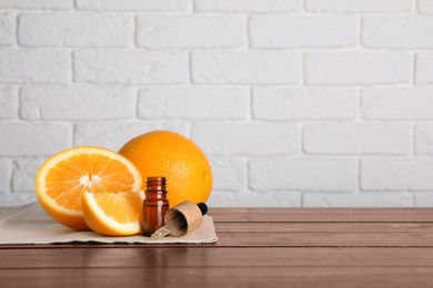 Bottle of essential oil with oranges on wooden table against white brick wall. Space for text