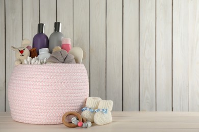 Photo of Basket with baby cosmetics and accessories on white wooden table. Space for text