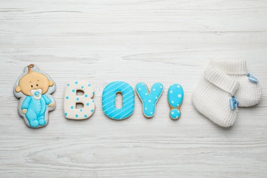 Word Boy made of tasty cookies near booties on white wooden table, flat lay. Baby shower party