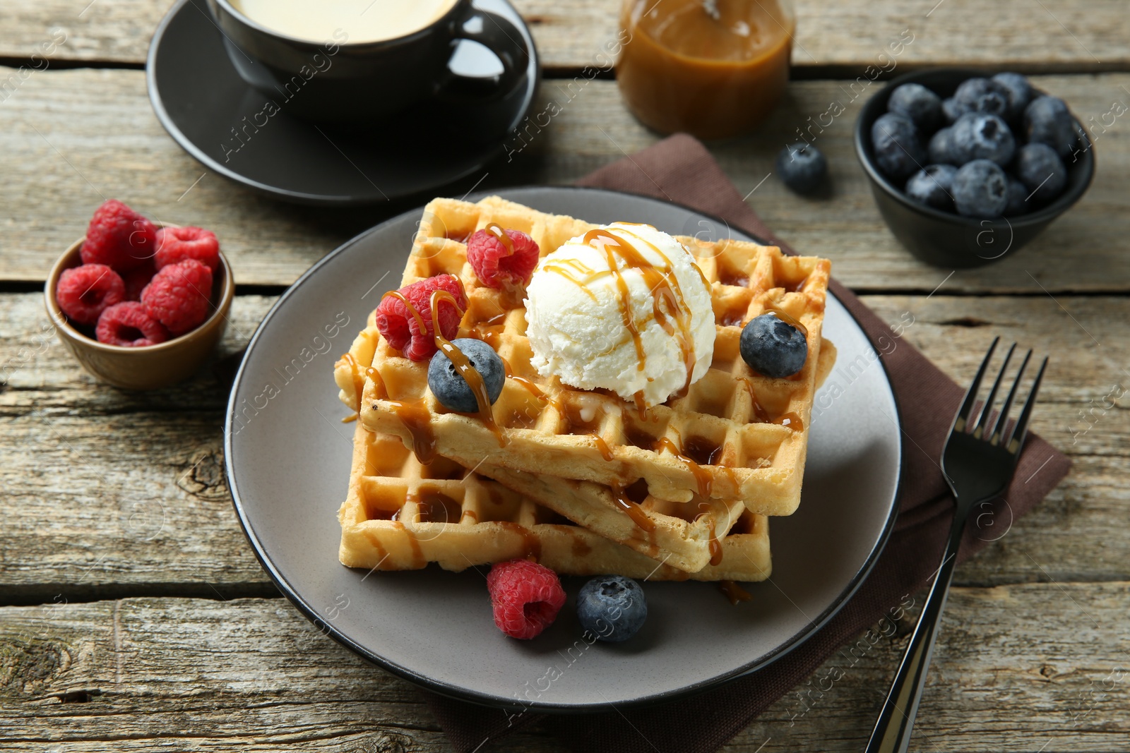 Photo of Delicious Belgian waffles with ice cream, berries and caramel sauce on wooden table