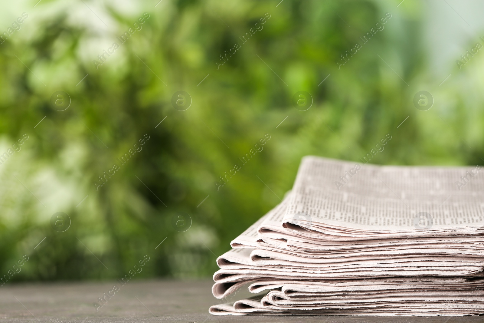 Photo of Stack of newspapers on grey table against blurred green background, space for text. Journalist's work