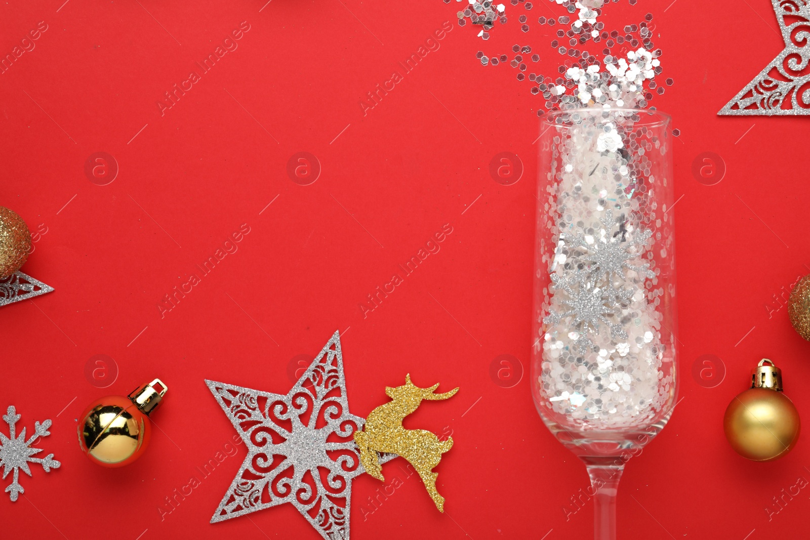 Photo of Flat lay composition with shiny confetti spilled out of champagne glass near Christmas decorations on red background, space for text