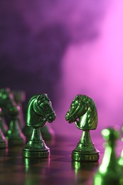 Two knights and other chess pieces on checkerboard in color light, selective focus. Space for text
