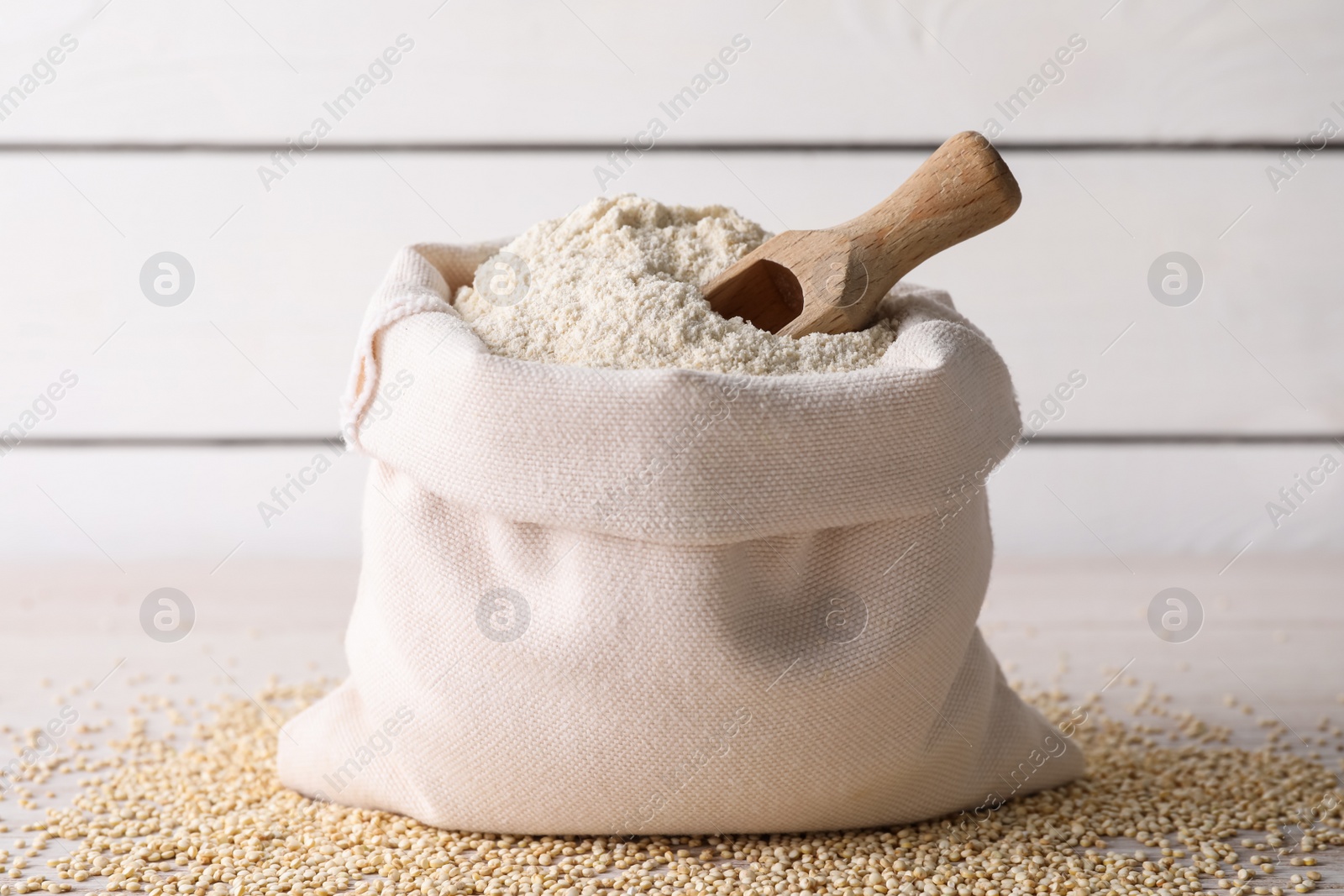 Photo of Sack with quinoa flour, scoop and seeds on white wooden table