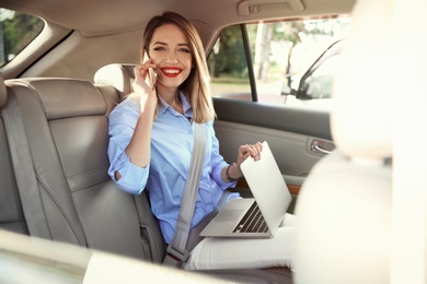 Photo of Young businesswoman with smartphone and laptop in car