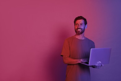 Image of Handsome man with laptop in neon lights, space for text