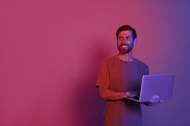 Handsome man with laptop in neon lights, space for text