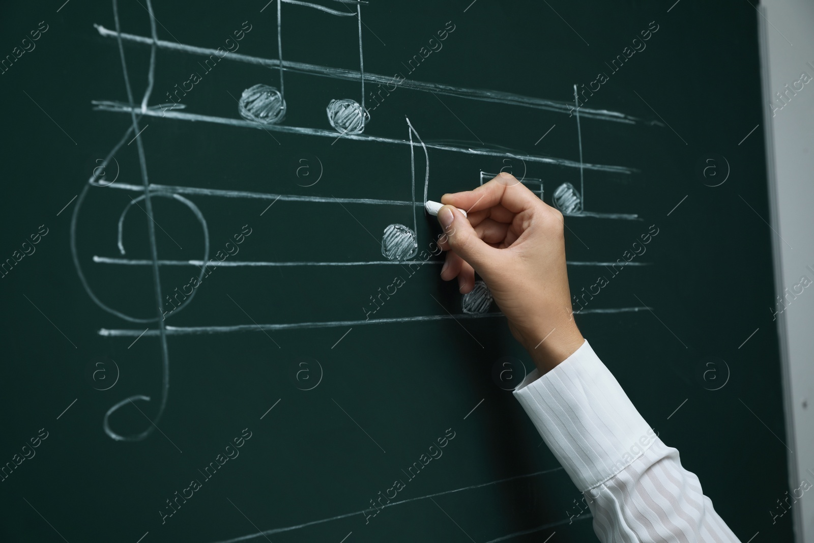 Photo of Teacher writing music notes with chalk on greenboard, closeup