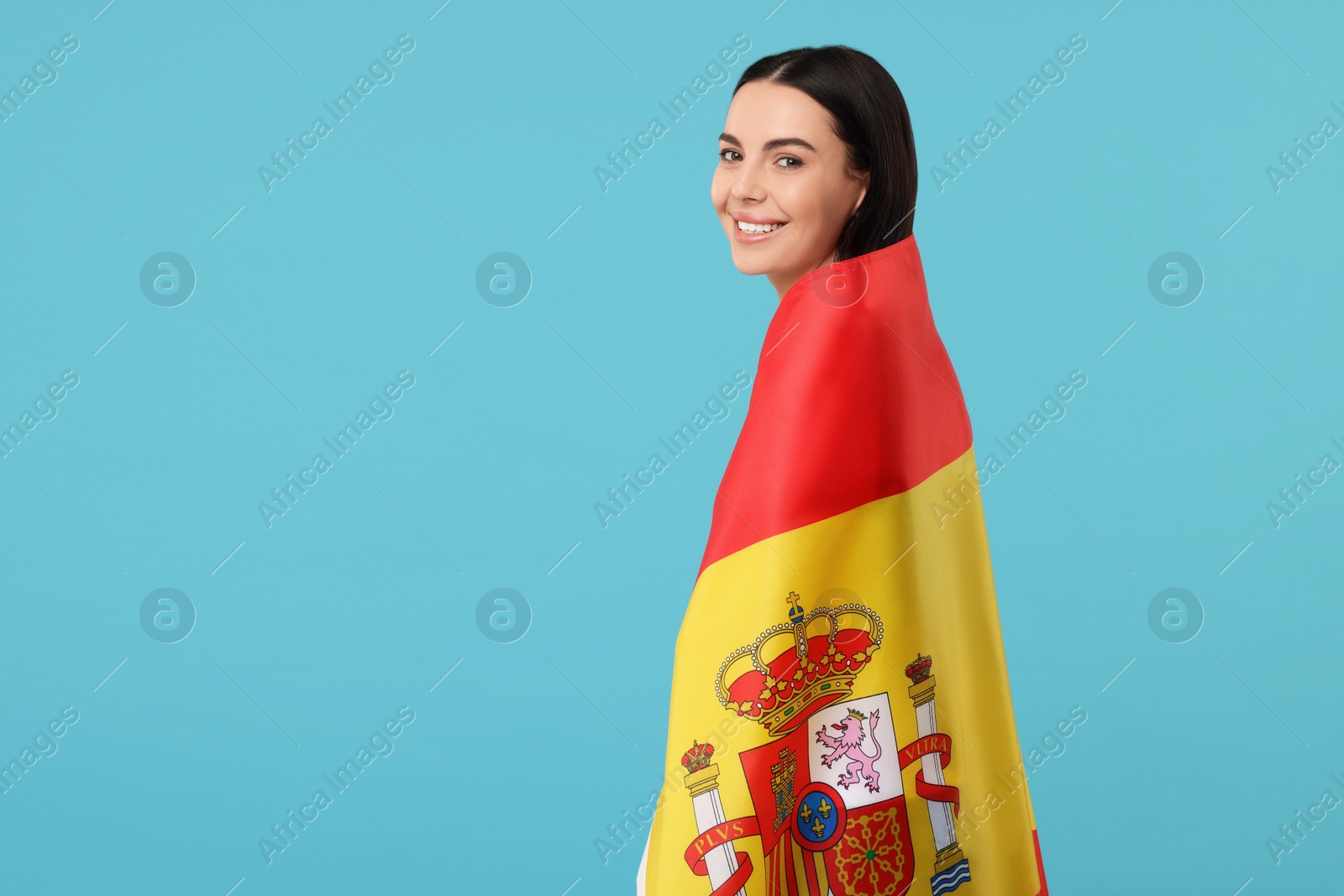 Photo of Happy young woman with flag of Spain on light blue background, space for text