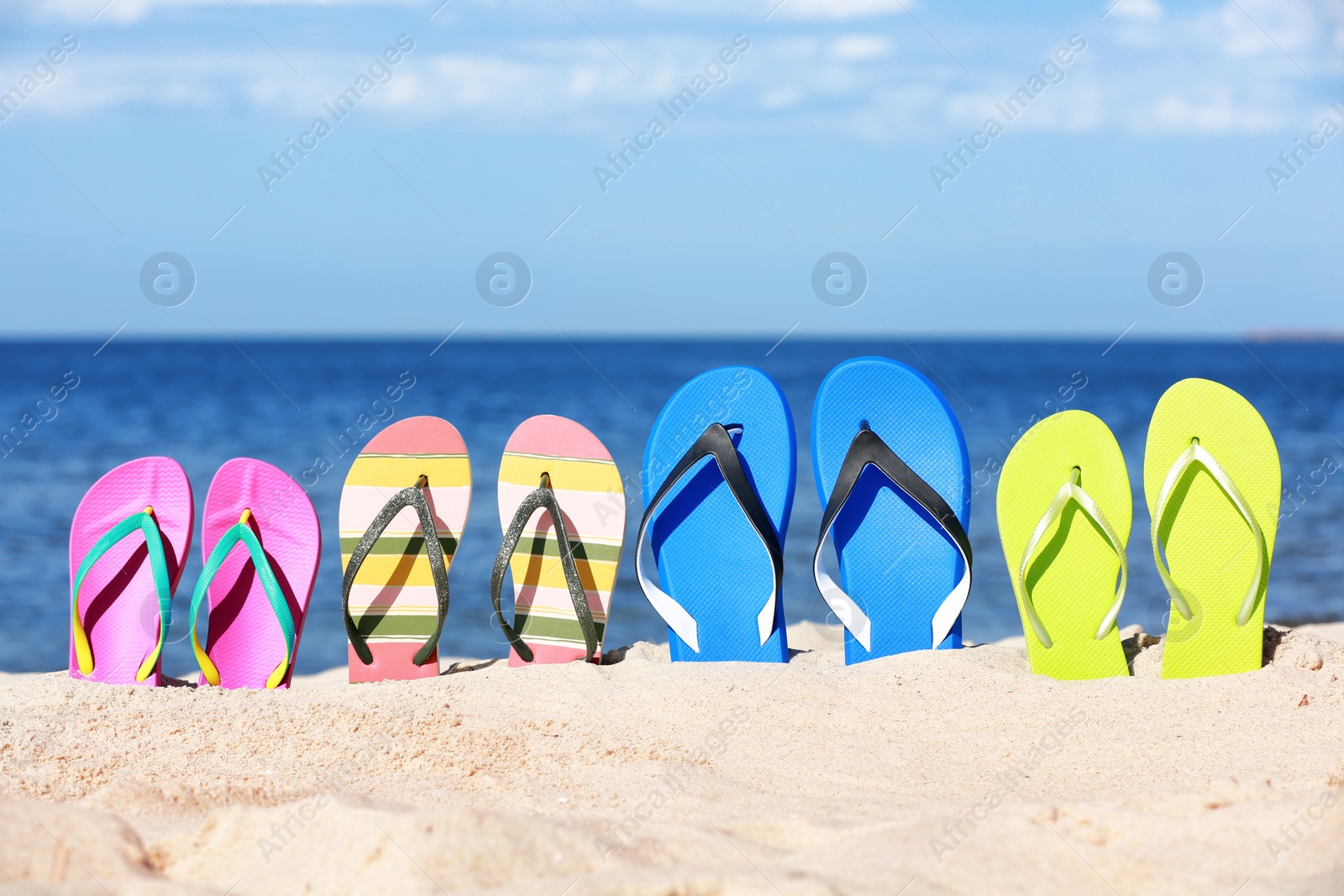 Photo of Composition with bright flip flops on sand near sea in summer. Beach accessories