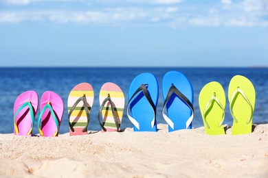 Photo of Composition with bright flip flops on sand near sea in summer. Beach accessories