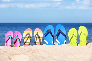 Composition with bright flip flops on sand near sea in summer. Beach accessories