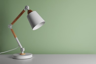 Photo of Stylish modern desk lamp on white table near light green wall, space for text