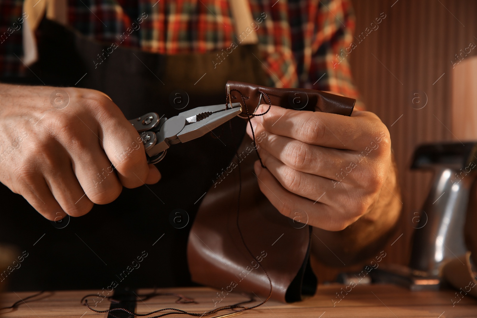 Photo of Man sewing piece of leather at table, closeup
