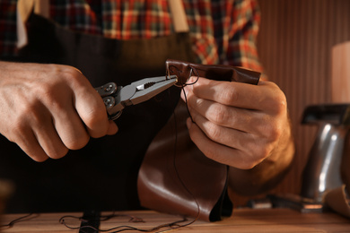 Man sewing piece of leather at table, closeup