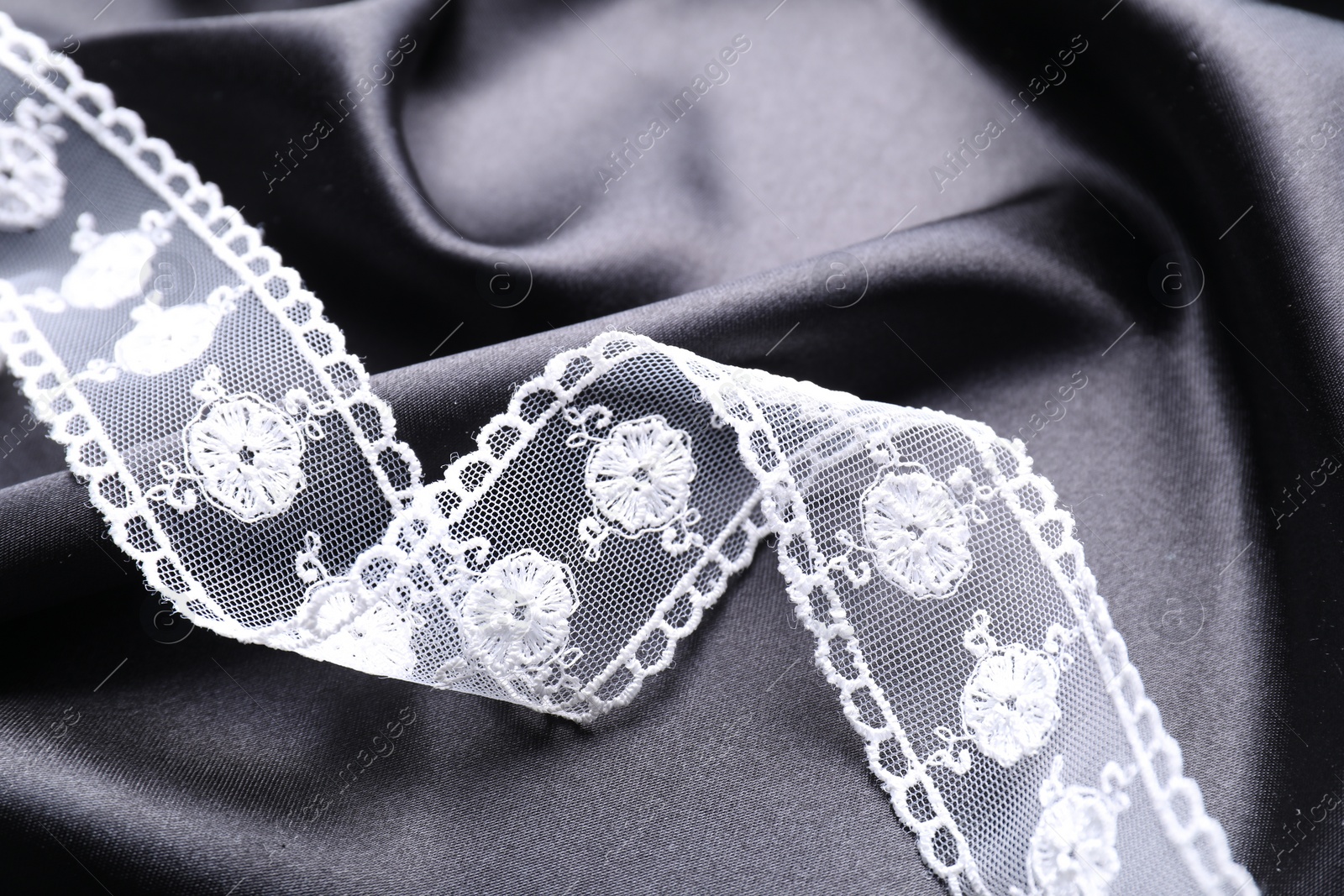 Photo of Beautiful white lace on black fabric, top view