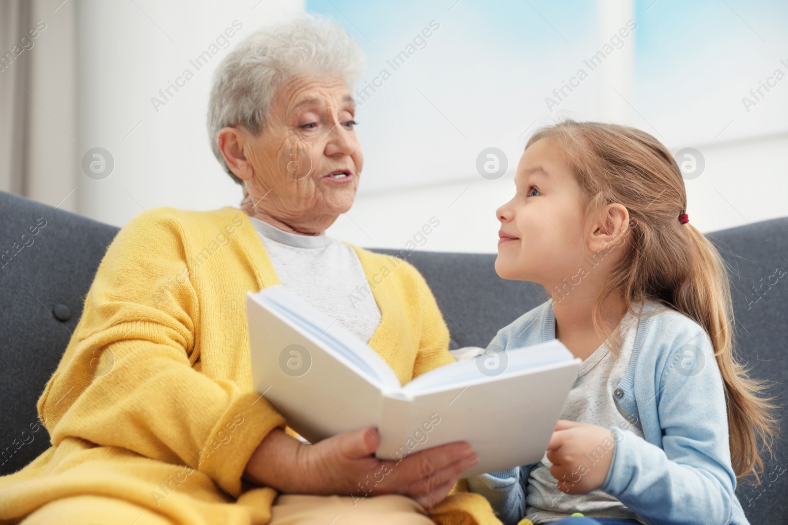 Photo of Cute girl and her grandmother reading book at home