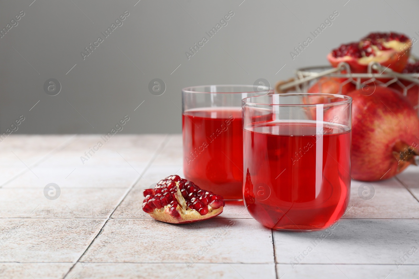 Photo of Tasty pomegranate juice in glasses and fresh fruits on white tiled table. Space for text