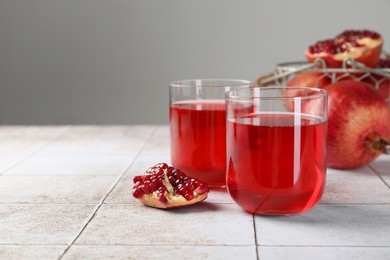 Photo of Tasty pomegranate juice in glasses and fresh fruits on white tiled table. Space for text