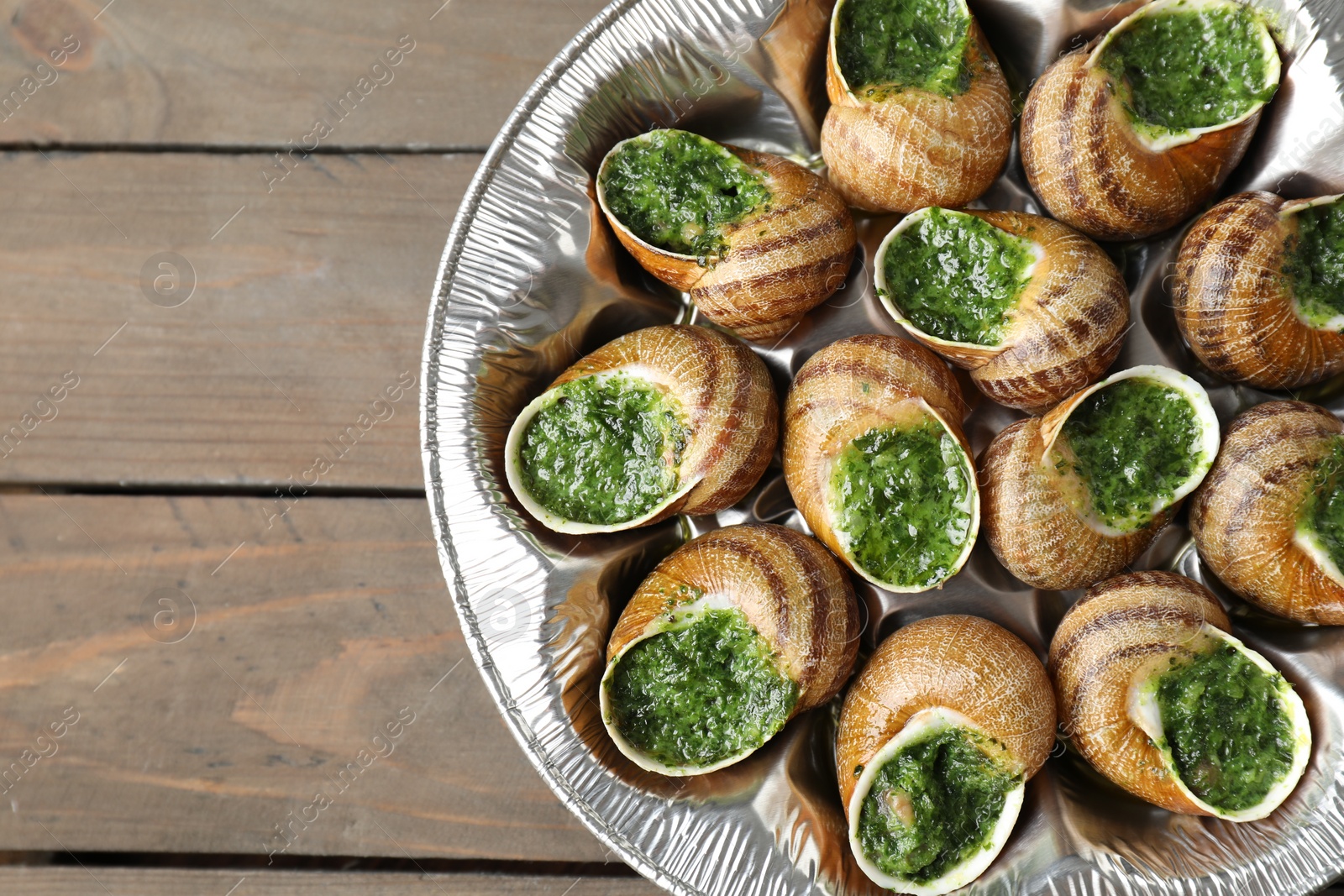 Photo of Delicious cooked snails on wooden table, top view. Space for text