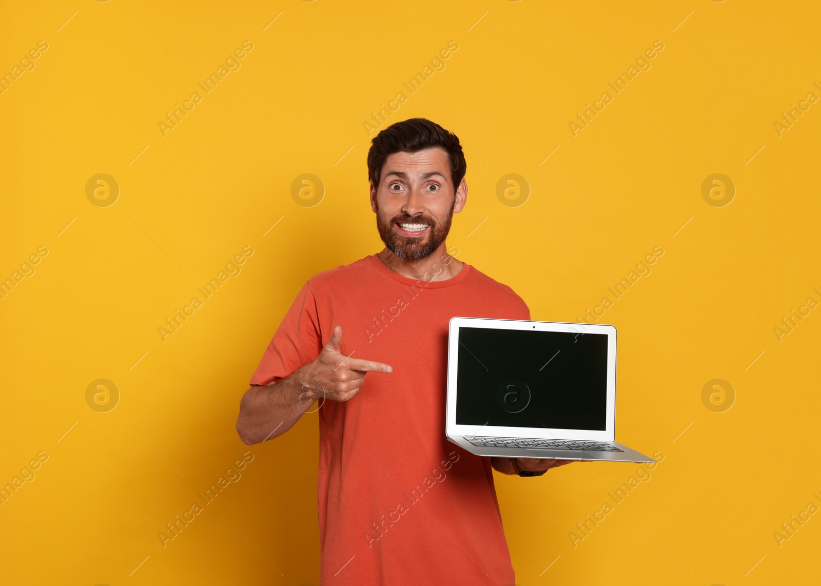 Photo of Handsome man with laptop on orange background