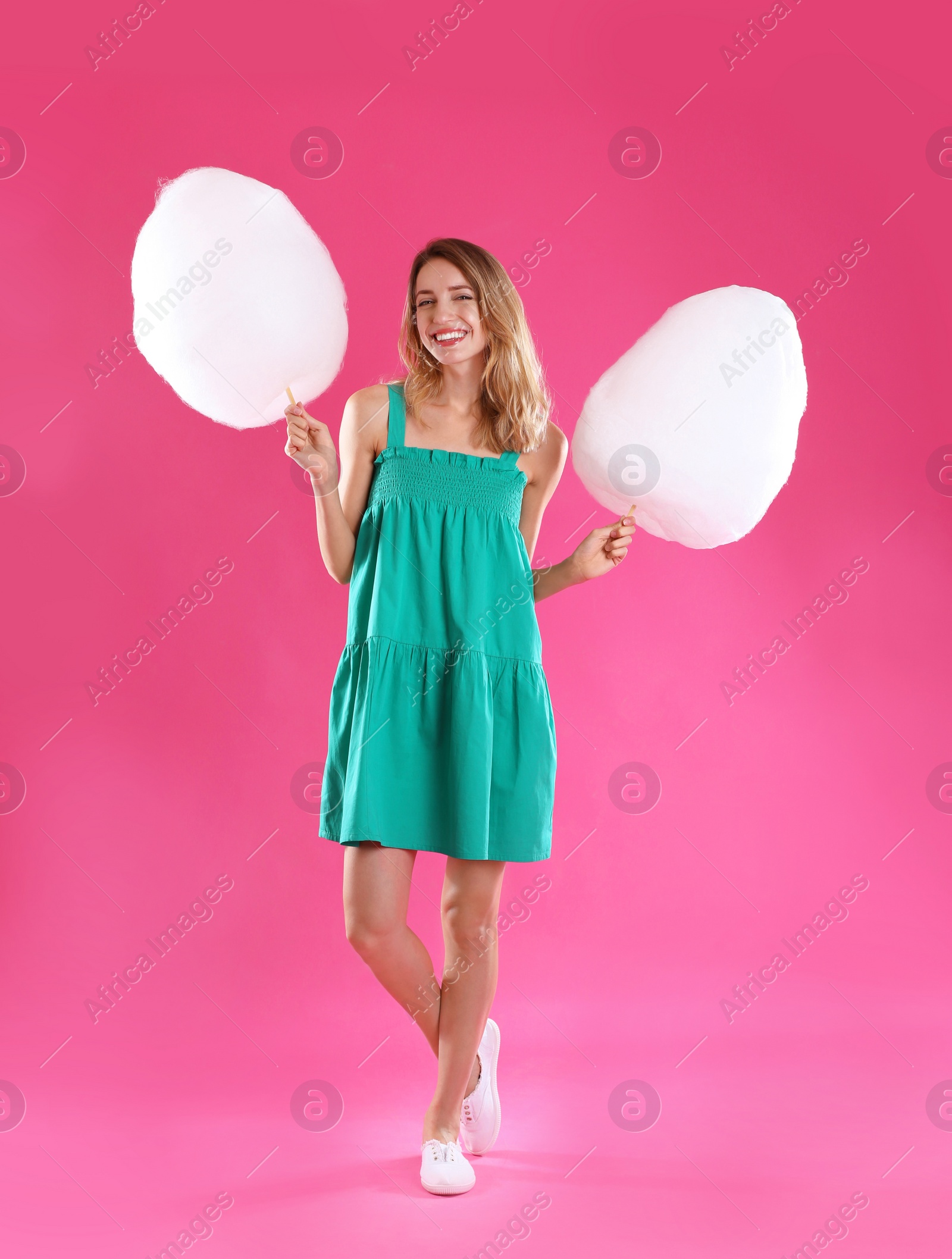 Photo of Happy young woman with cotton candies on pink background