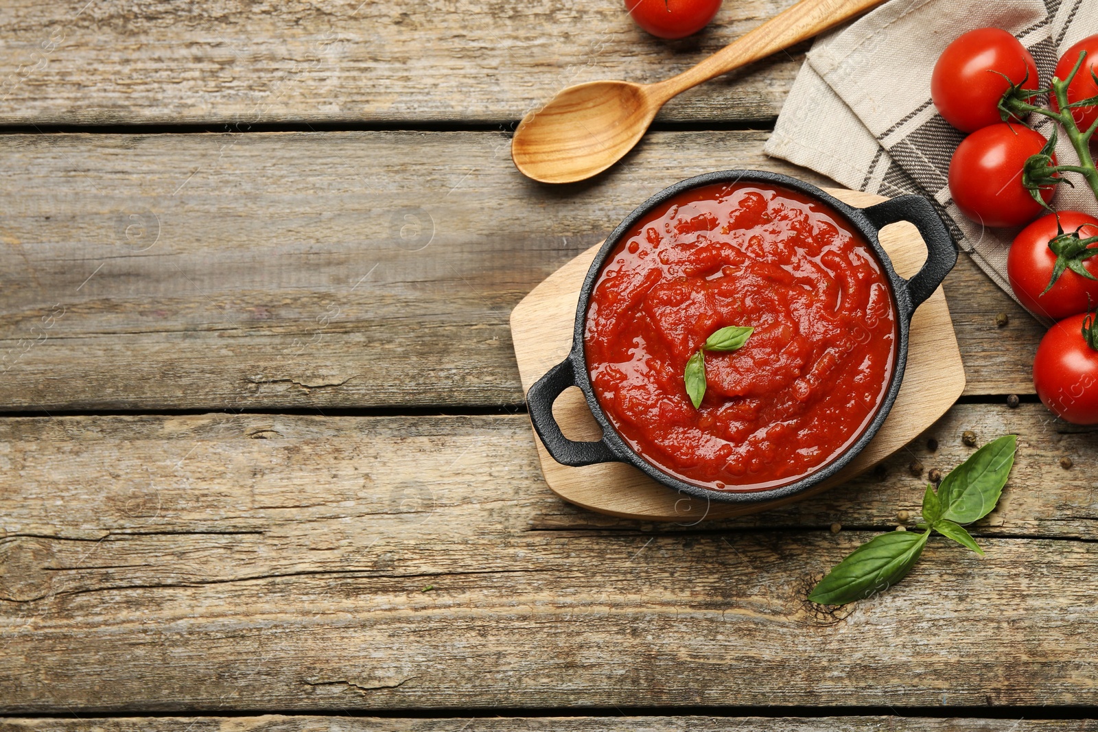 Photo of Homemade tomato sauce in bowl, spoon and fresh ingredients on wooden table, flat lay. Space for text