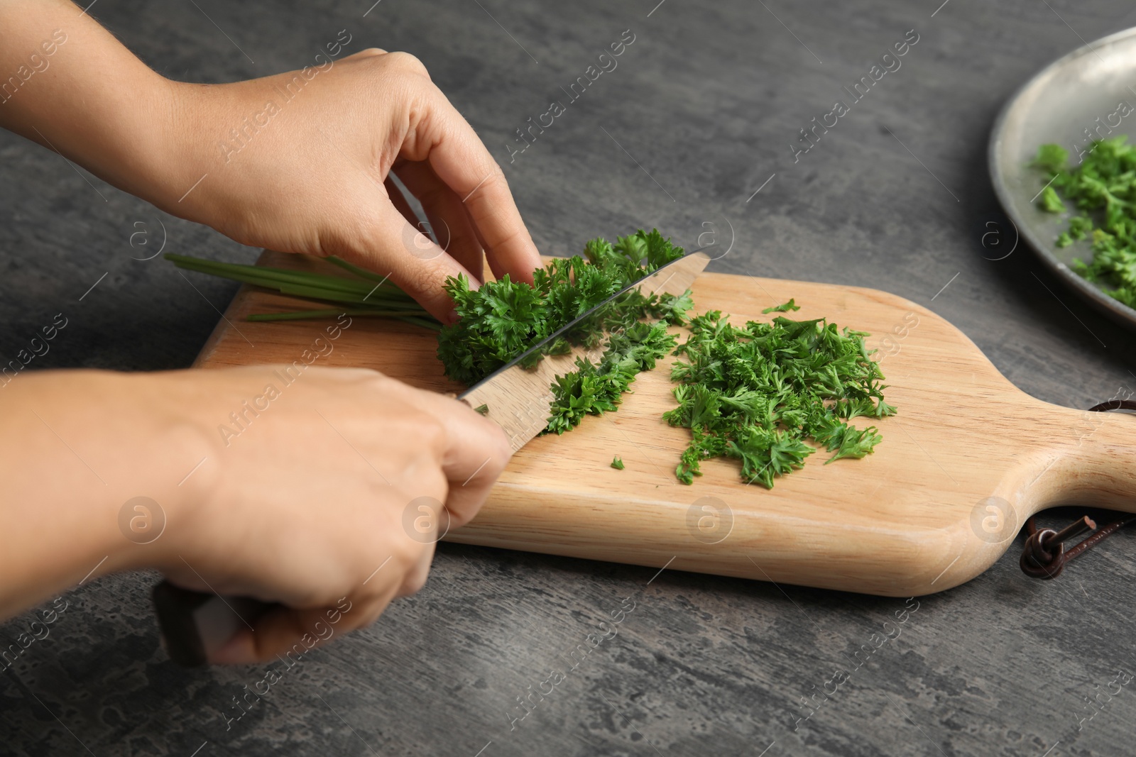 Photo of Woman cutting fresh green parsley on wooden board, closeup