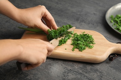 Photo of Woman cutting fresh green parsley on wooden board, closeup