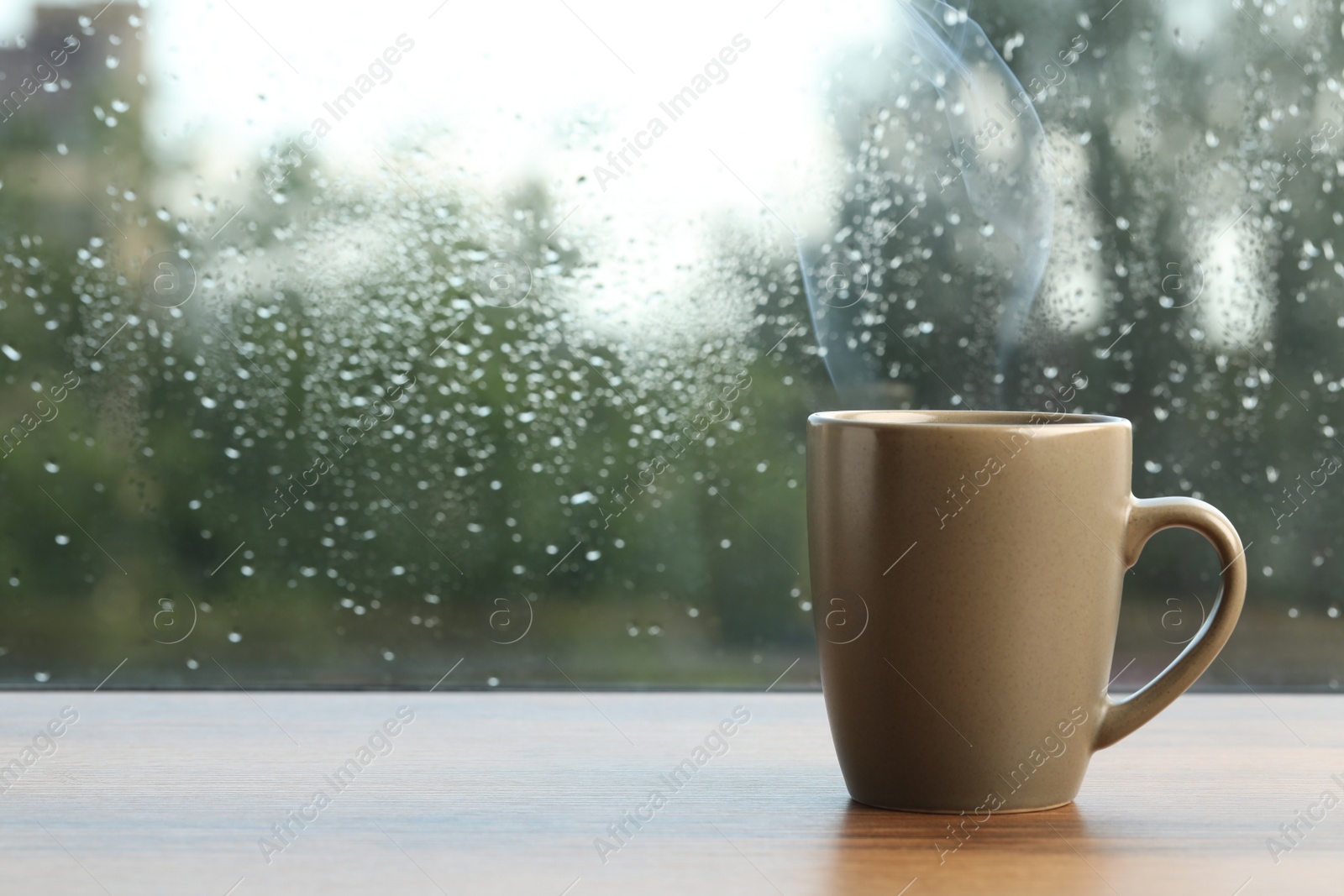 Photo of Cup of hot drink near window on rainy day. Space for text