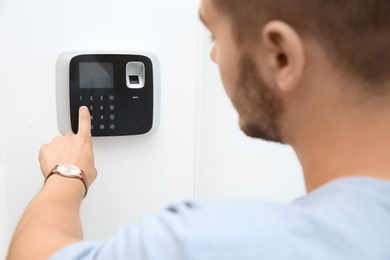 Young man entering code on alarm system keypad indoors