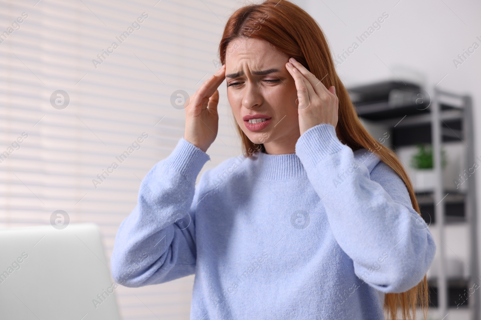 Photo of Woman suffering from headache at workplace in office