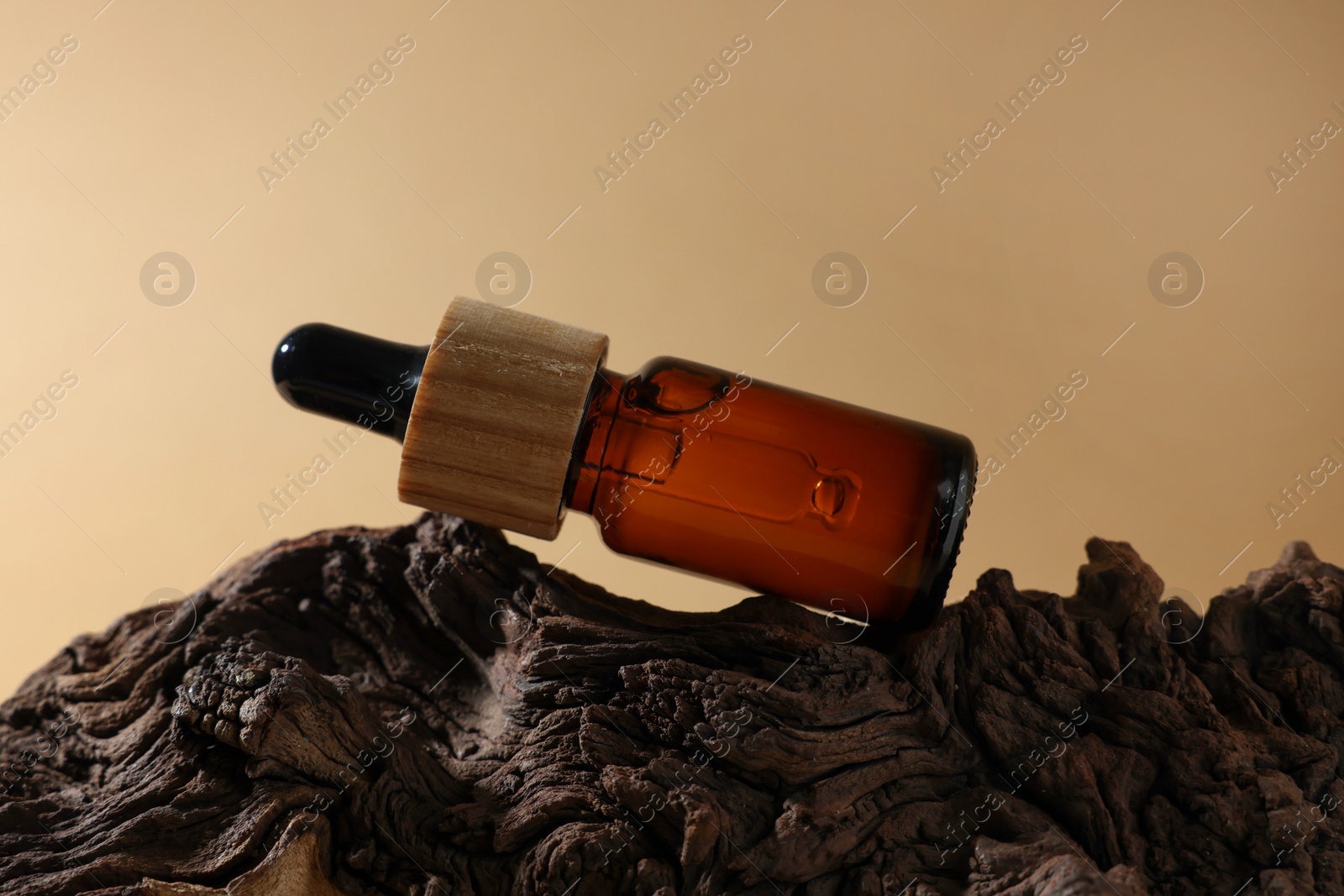 Photo of Bottle of essential oil on tree bark against dark beige background