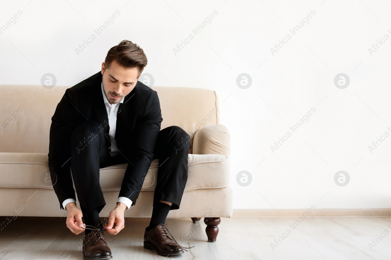 Photo of Young man putting on elegant leather shoes indoors