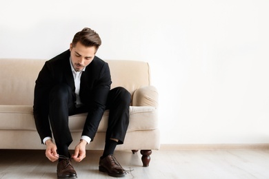 Photo of Young man putting on elegant leather shoes indoors