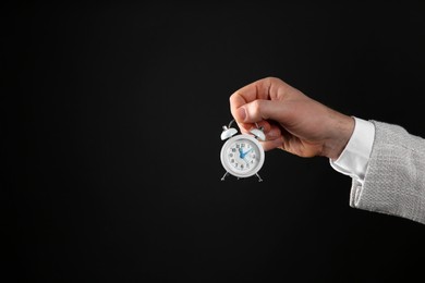 Photo of Closeup view of businessman holding tiny alarm clock on black background, space for text. Time management
