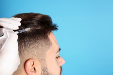 Young man with hair loss problem receiving injection on color background, closeup. Space for text