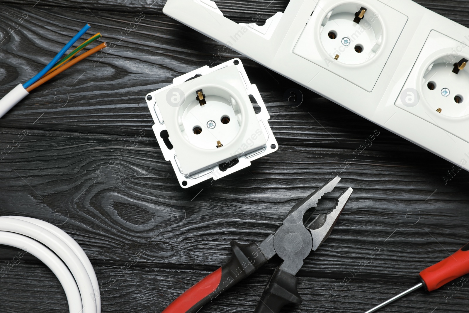 Photo of Set of electrician's tools and power sockets on black wooden table, flat lay