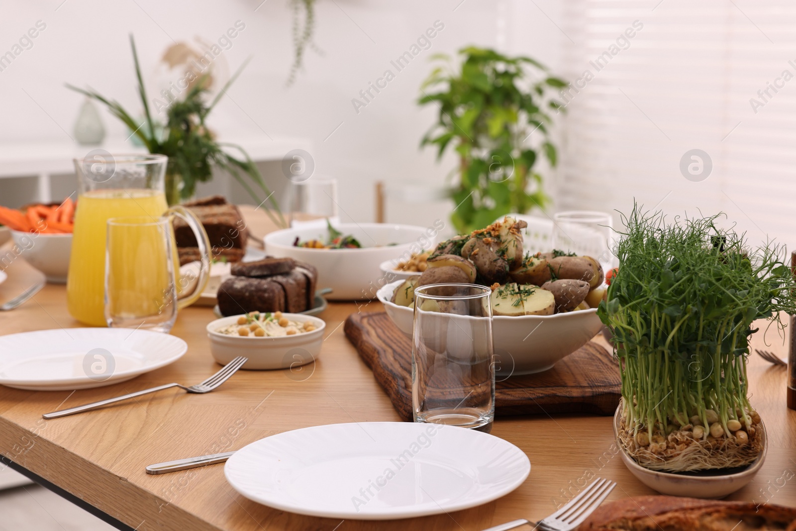 Photo of Healthy vegetarian food, jug of juice, cutlery, glasses and plates on wooden table indoors