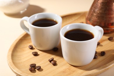 Delicious coffee in cups and beans on beige table, closeup