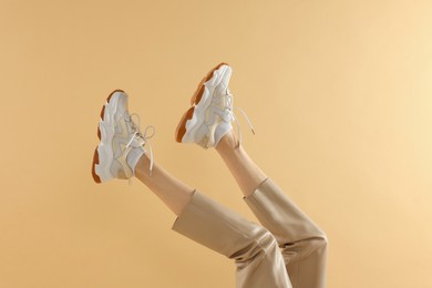 Photo of Woman wearing pair of new stylish sneakers on beige background, closeup